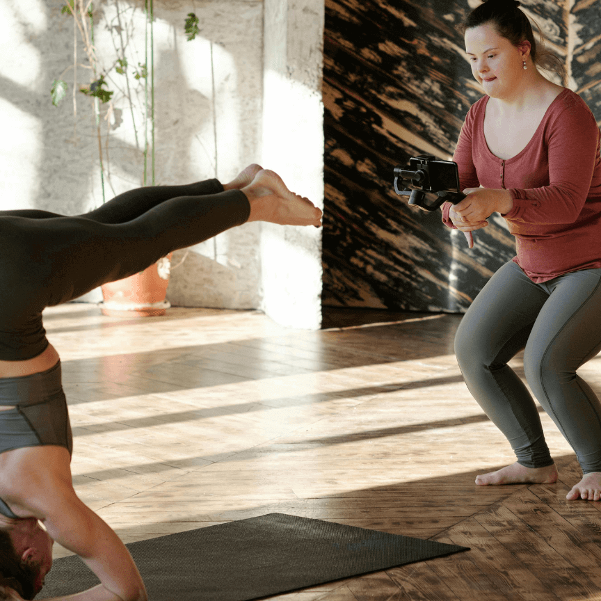 woman filming another woman doing yoga who is holding a headstand-based pose